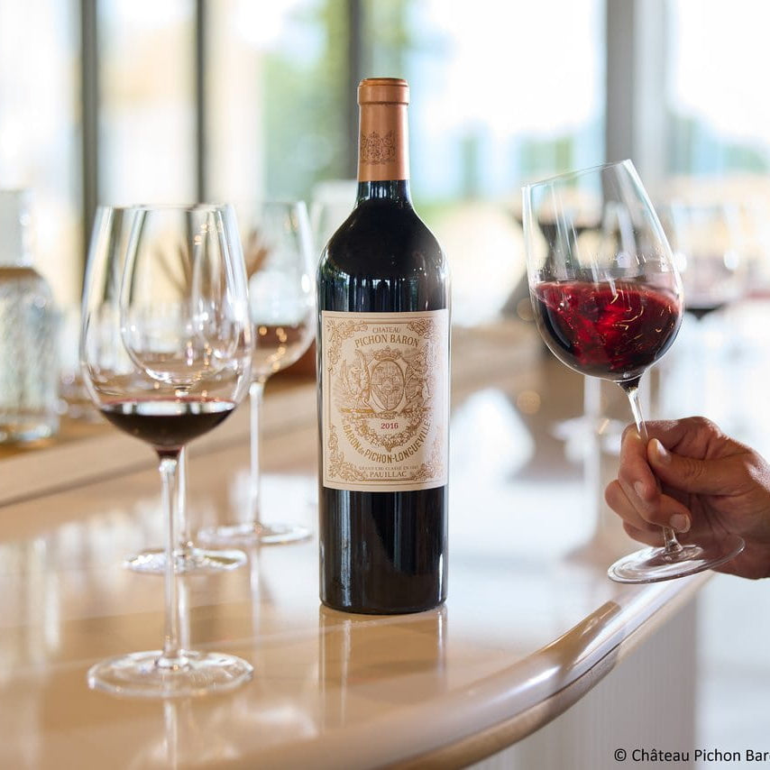 Bottle of Château Pichon Baron with two glasses of red wine on a table.