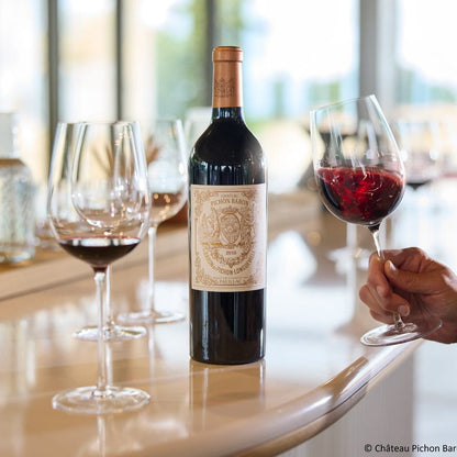 Bottle of Château Pichon Baron with two glasses of red wine on a table.